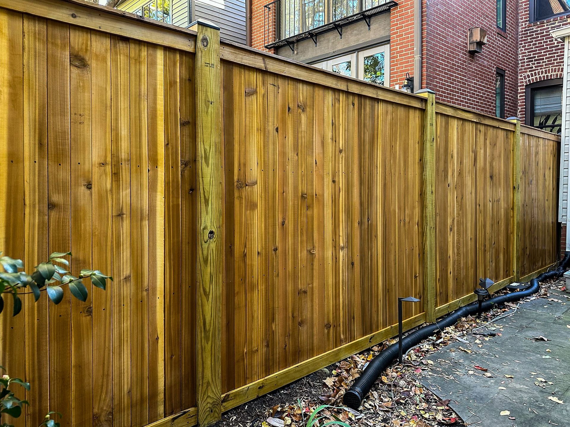 Wooden privacy fence along a walkway, brown with a ridged top.