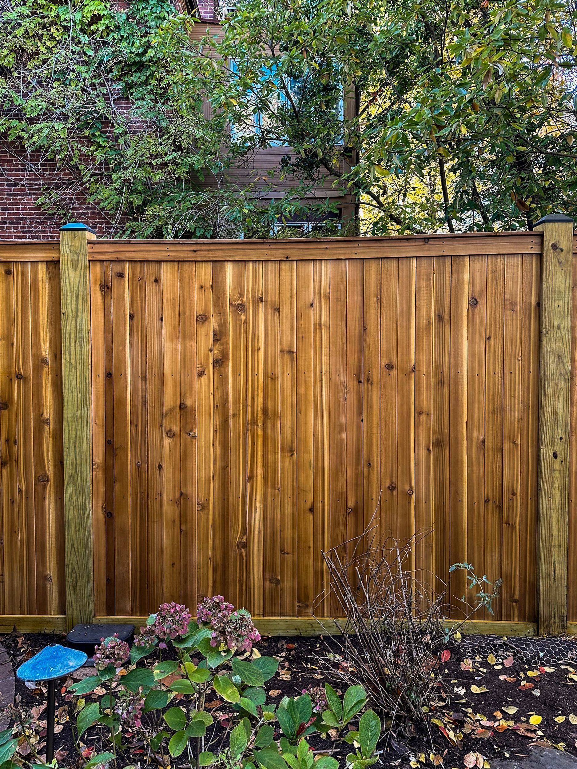 Wooden privacy fence in front of a brick wall and foliage.