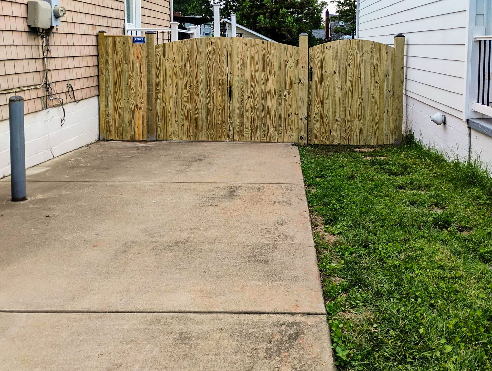Concrete patio with a wooden fence and gate, next to a grassy area and buildings.