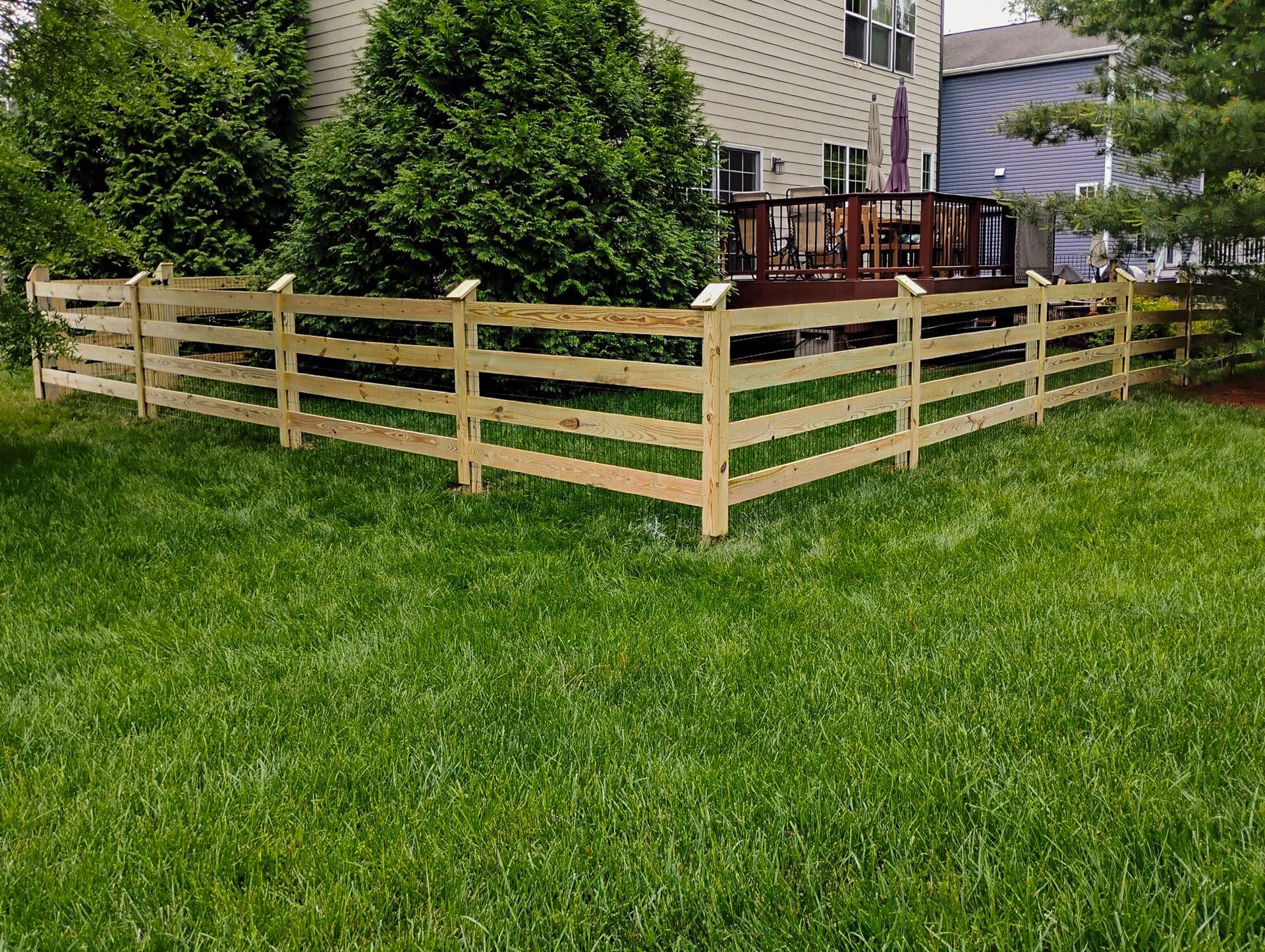 Wooden fence in a grassy yard, partially surrounding a house with a deck.