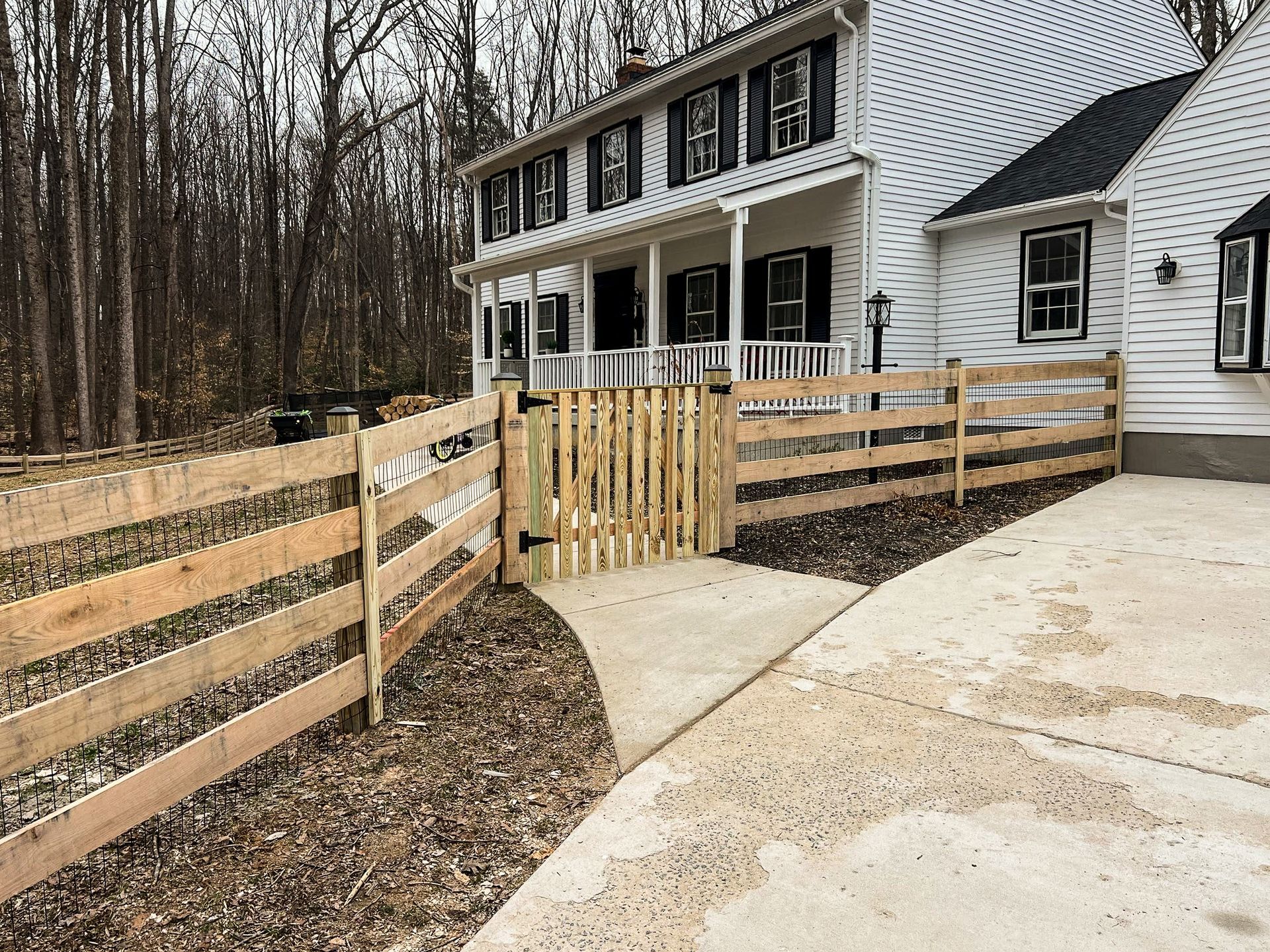 Wooden fence with a gate in front of a white house with black shutters.