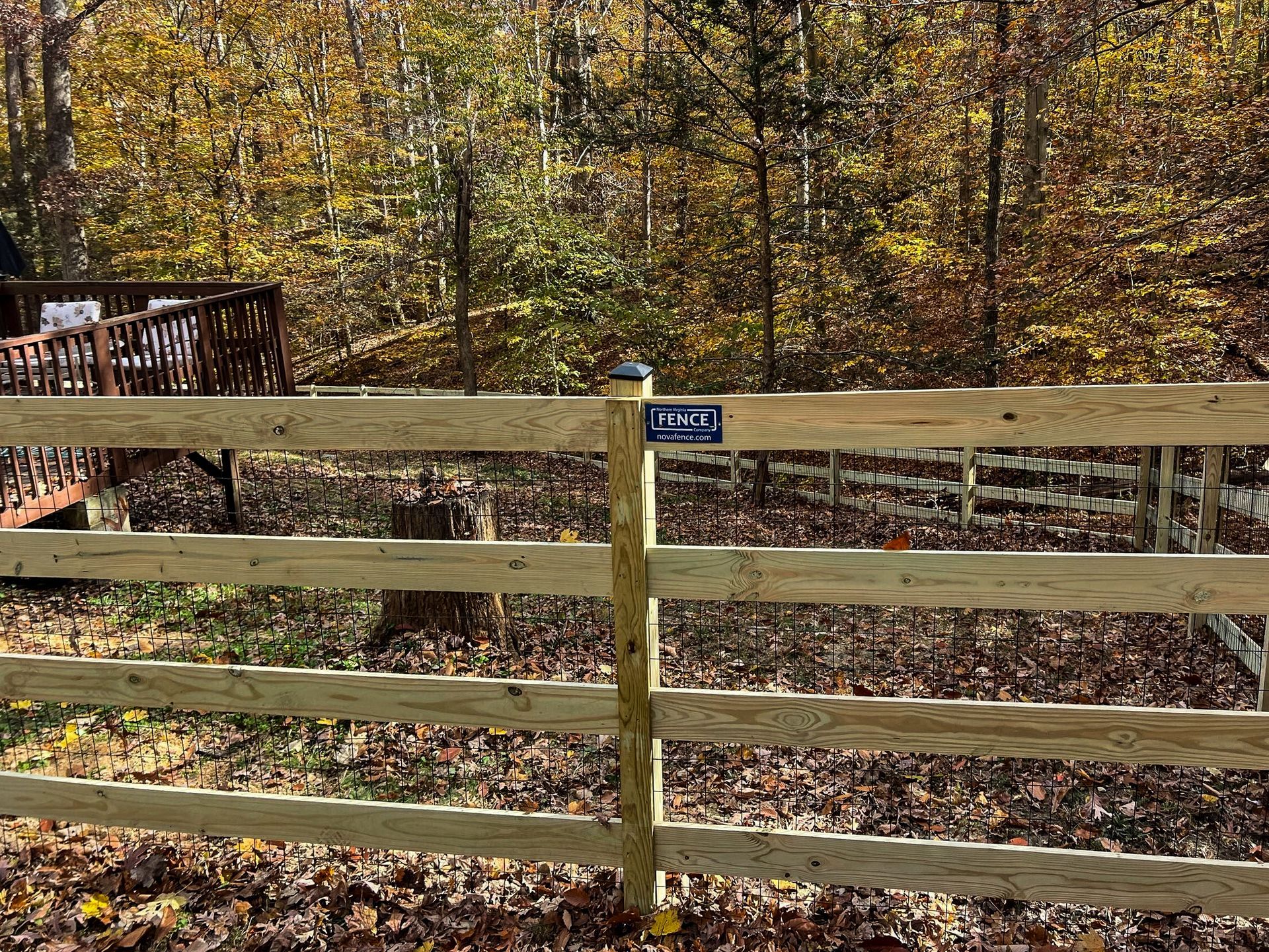 Wooden split-rail fence with a sign, surrounded by fall foliage. A deck is visible in the background.