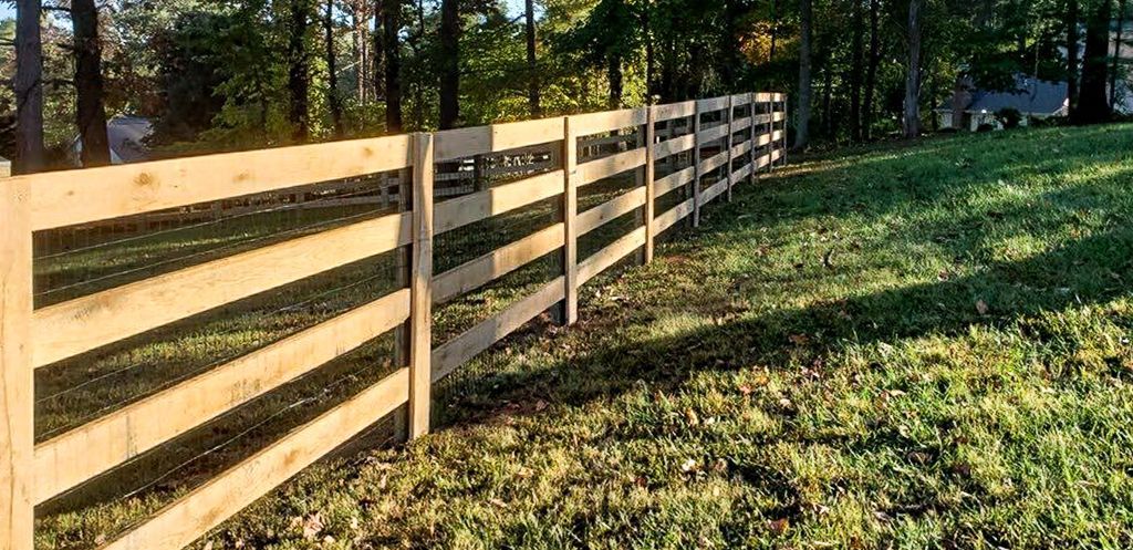Wooden fence in a grassy field with trees in the background.