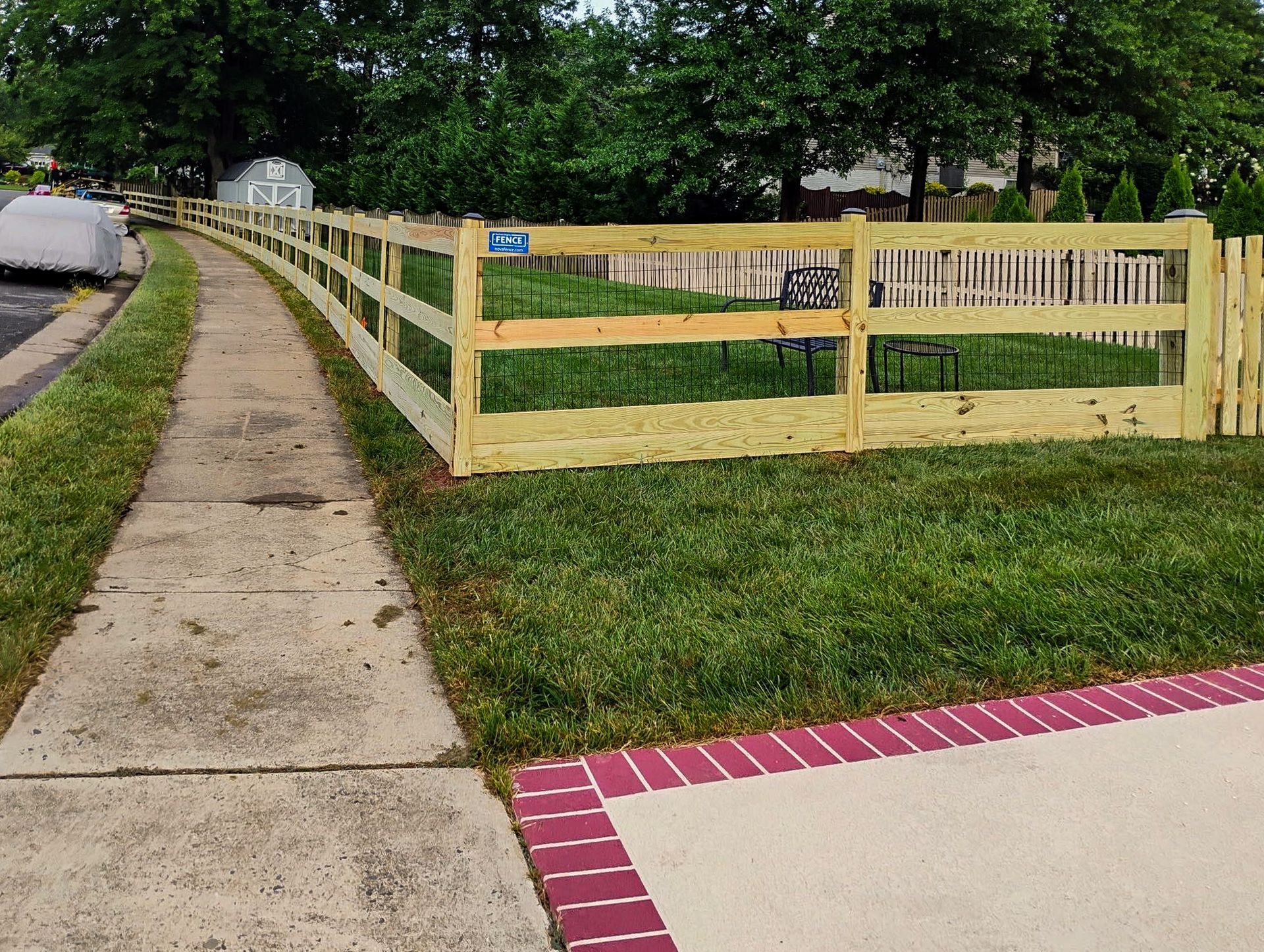 Wooden fence bordering a grassy yard next to a sidewalk and a red-bricked border.