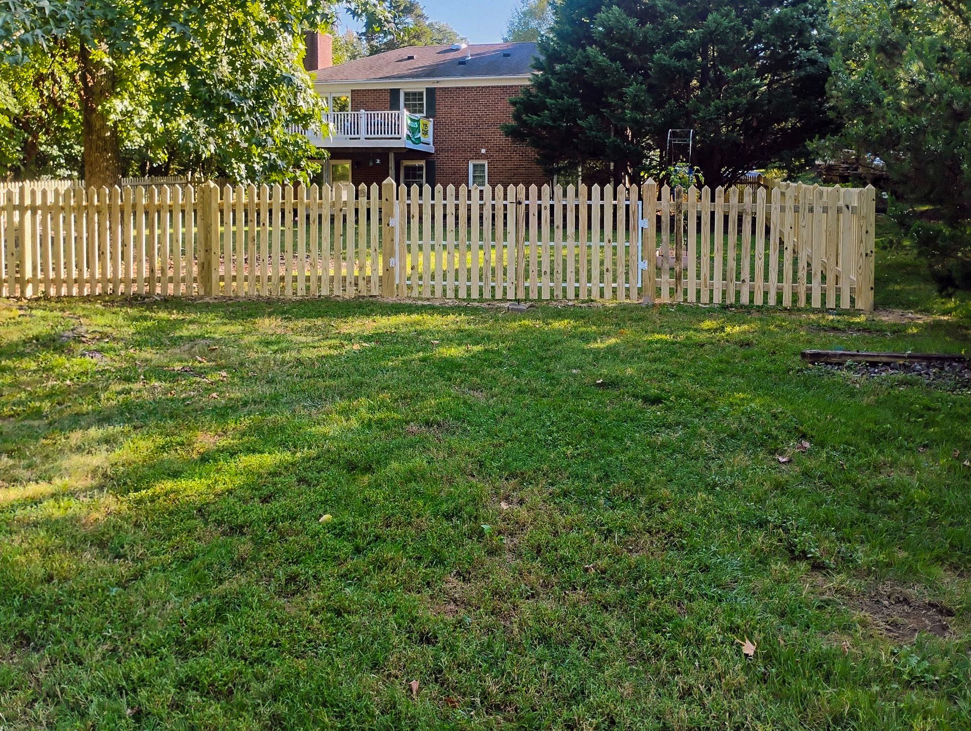 Wooden picket fence encloses a grassy backyard; a house is in the background.