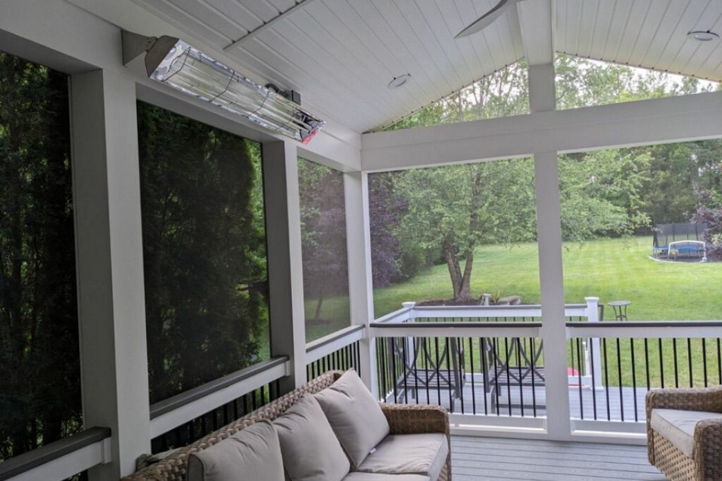 Screened-in porch with wicker furniture and a heating lamp, overlooking a green yard and trees.