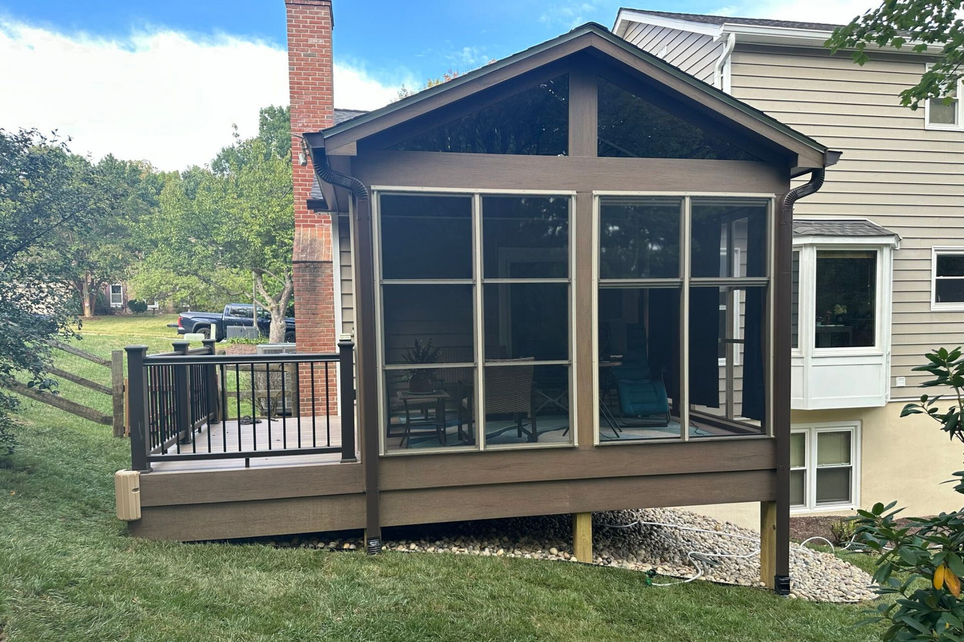 Screened-in porch and deck with a gable roof, brown siding, overlooking a yard.
