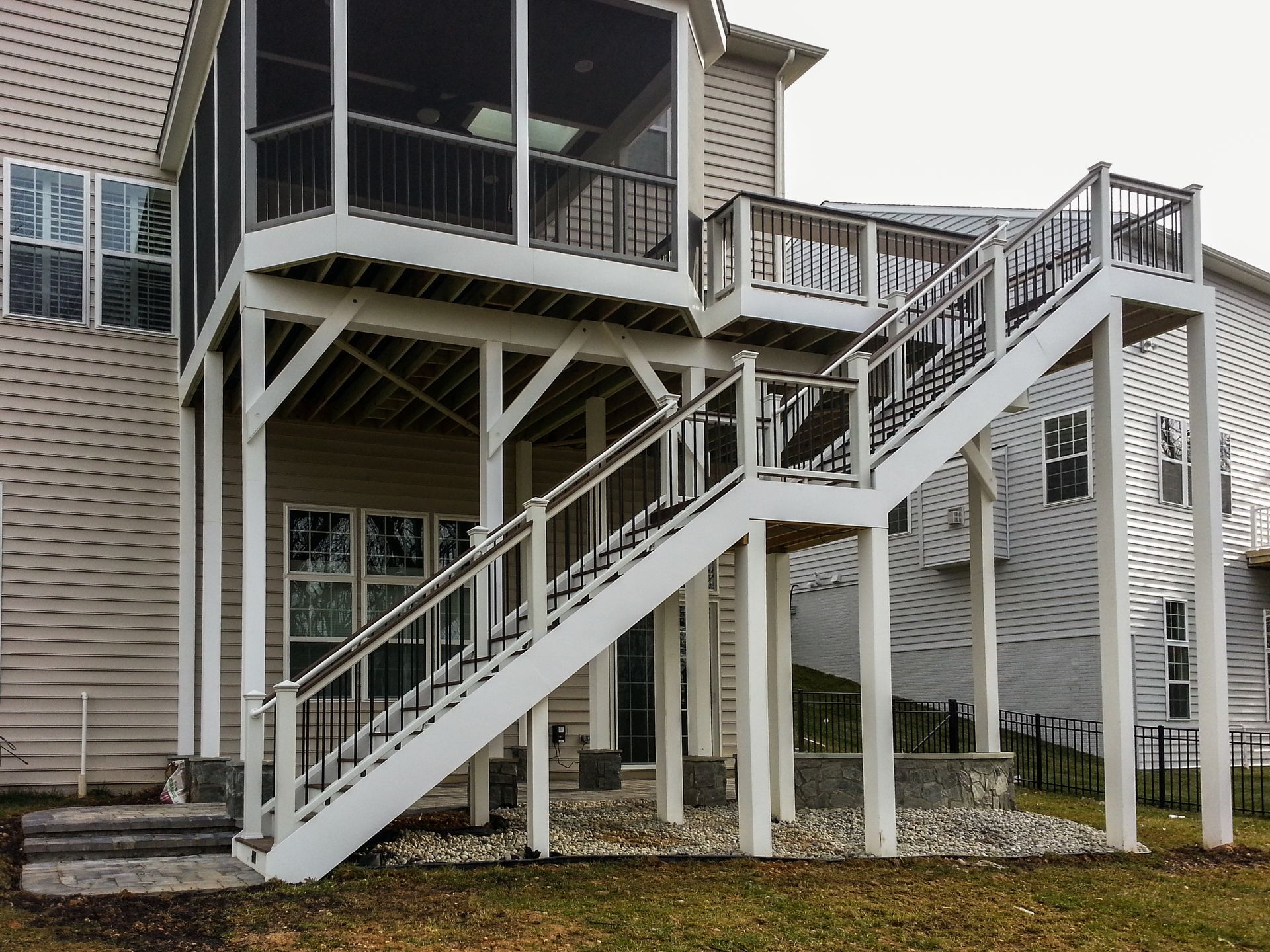 Two-story deck with stairs, white supports, black railings, attached to a light-colored house.