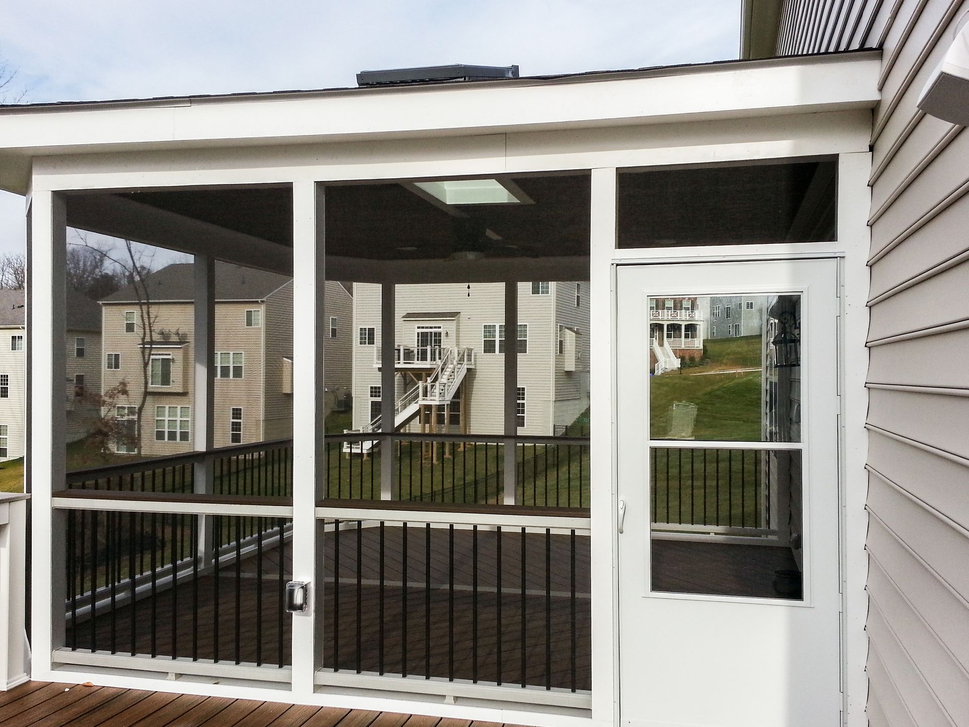 Screened-in porch with white trim, dark railing, and door, attached to a house with beige siding.
