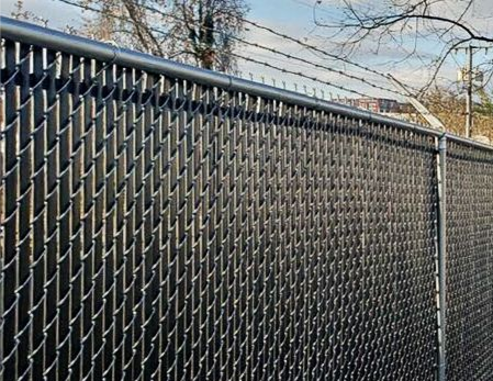 Chain link fence with black privacy slats and barbed wire on top.