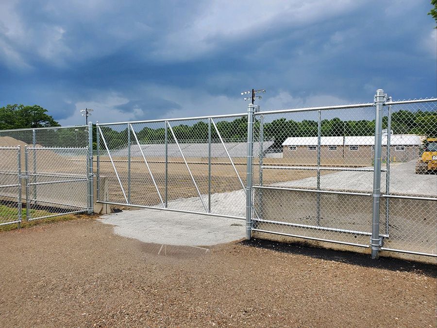 Open chain-link gate leading to a construction site with a cloudy sky overhead.