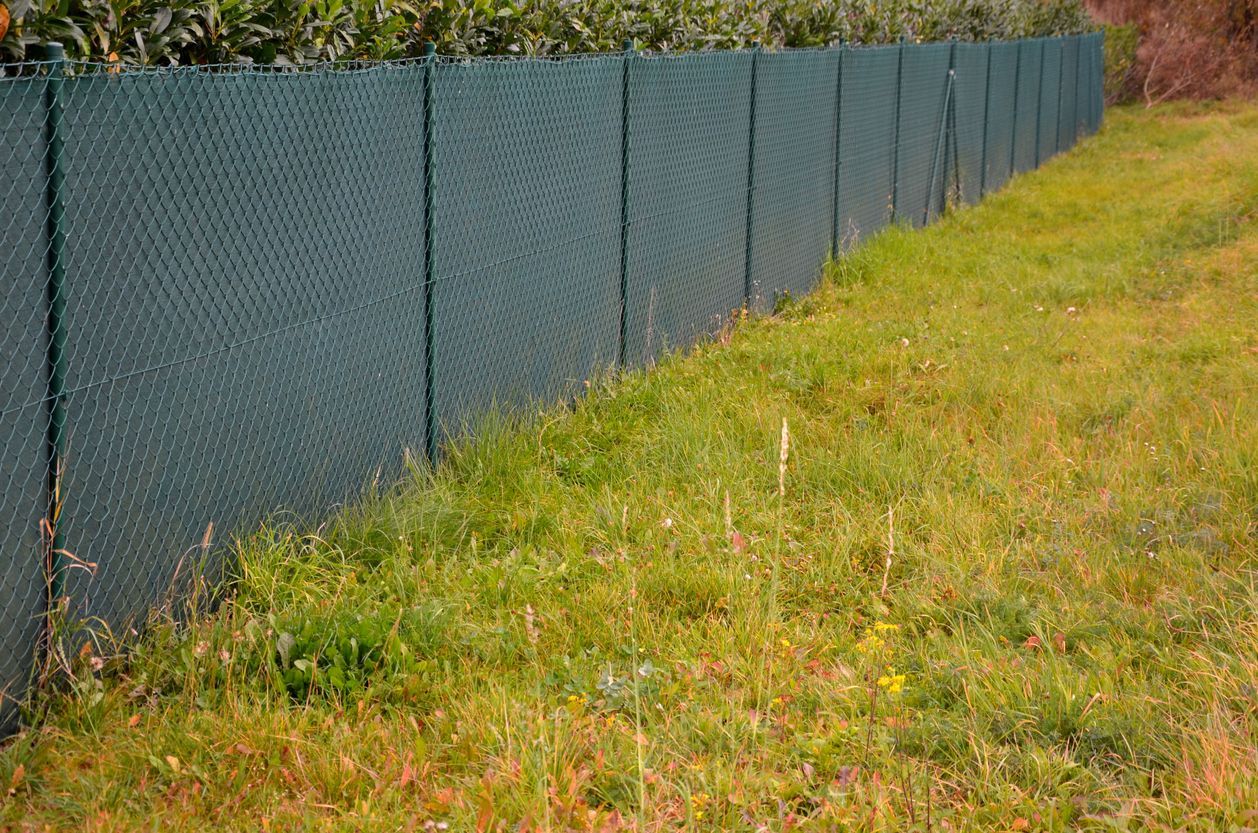 Green chain link fence with privacy slats, bordering a grassy area.