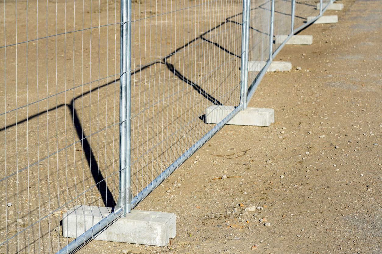 Metal fence on concrete blocks in a dirt area, casting a long shadow.