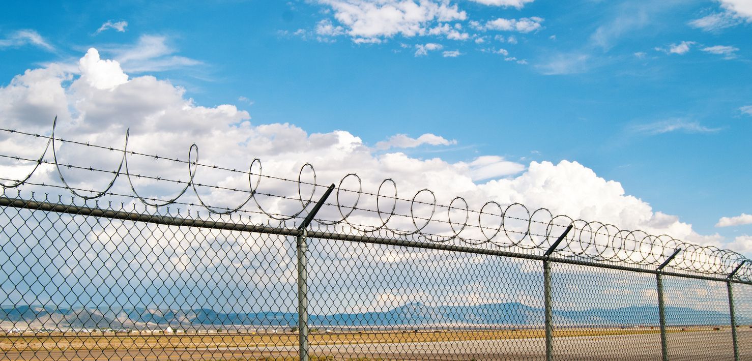 Chain link fence with razor wire, against a blue sky with clouds.