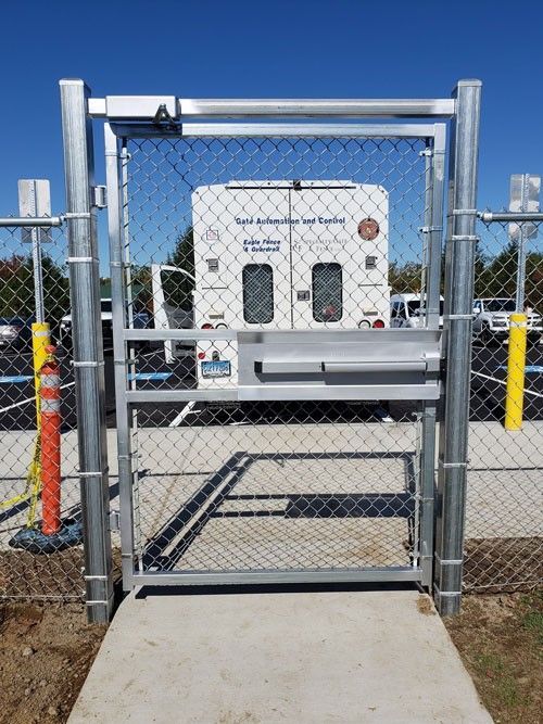 Metal chain-link gate on a concrete path with a truck visible in the background. Blue sky.