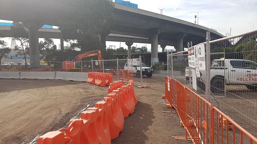Construction site under an overpass with orange barriers, machinery, and trucks.