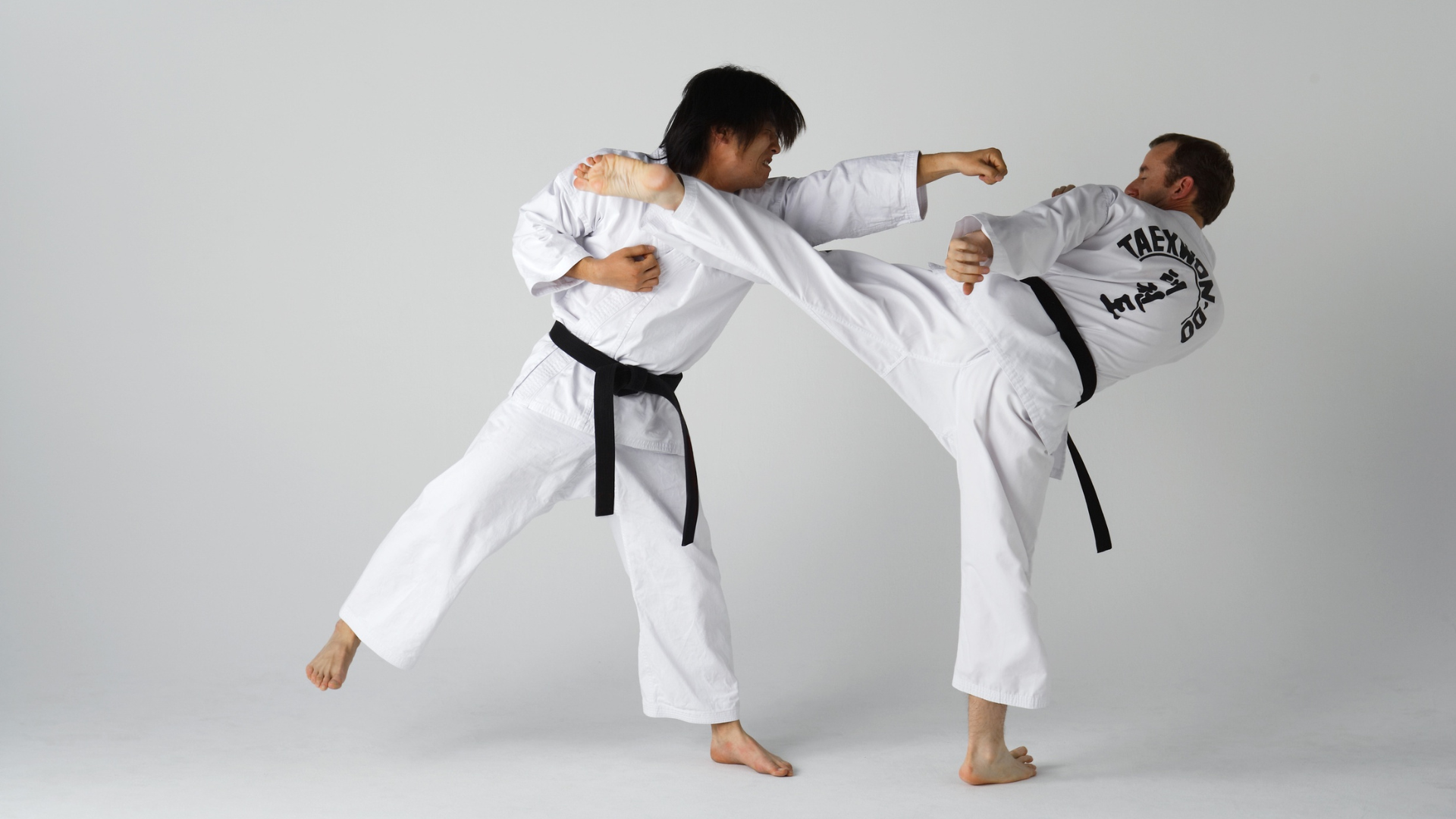 Two people in white martial arts uniforms, one kicking and punching.