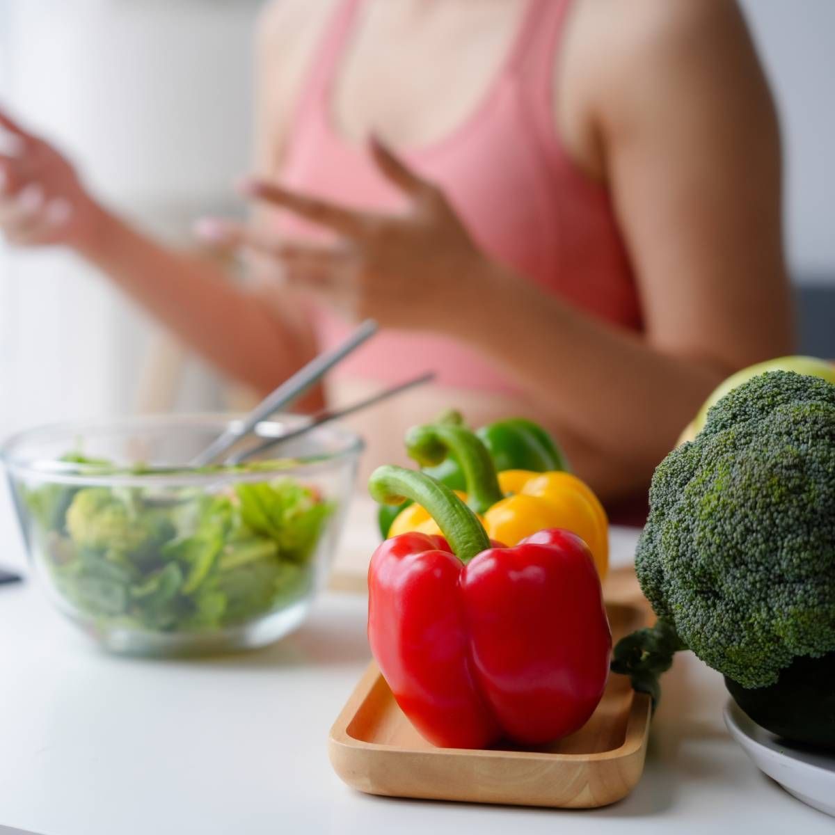 Woman preparing vegetables: red, yellow, and green bell peppers, broccoli, and a bowl of salad.