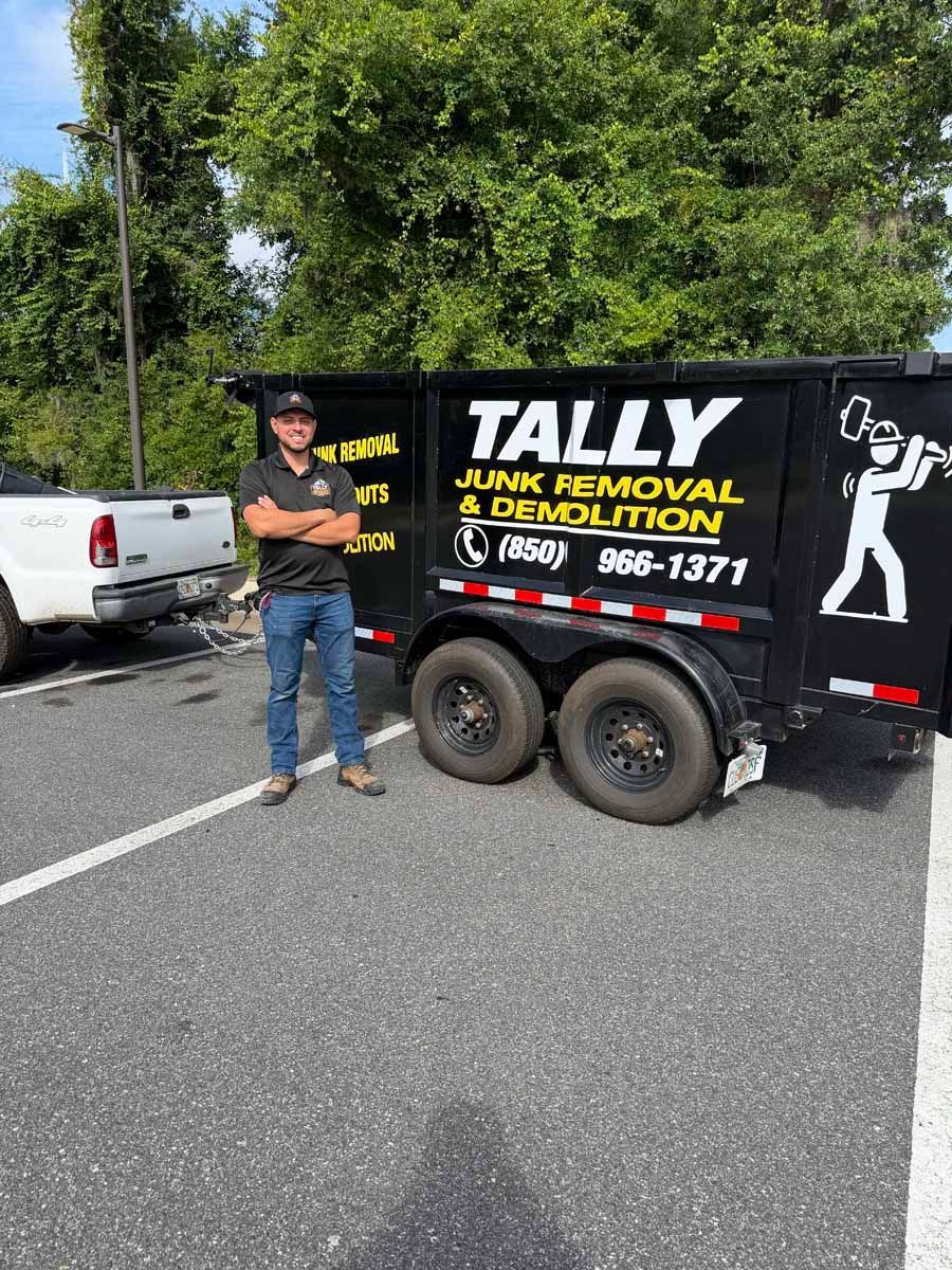 Man standing beside a black Tally Junk Removal trailer on a roadside