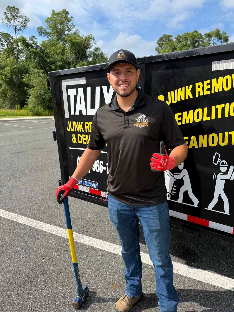 Man in black shirt and jeans holding a shovel and red gloves beside a junk removal truck.
