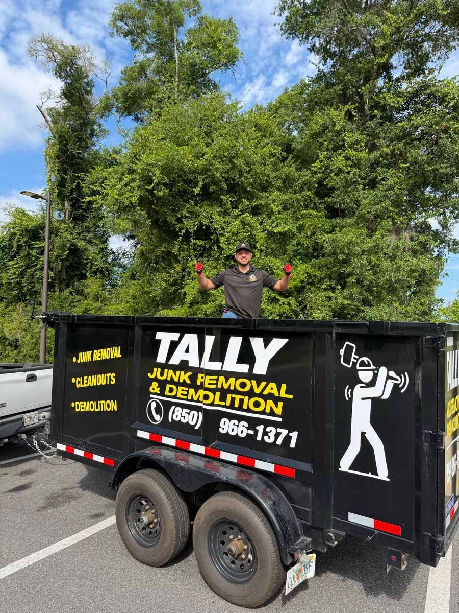 Black Tally Junk Removal & Demolition trailer with a worker standing on it by the roadside.