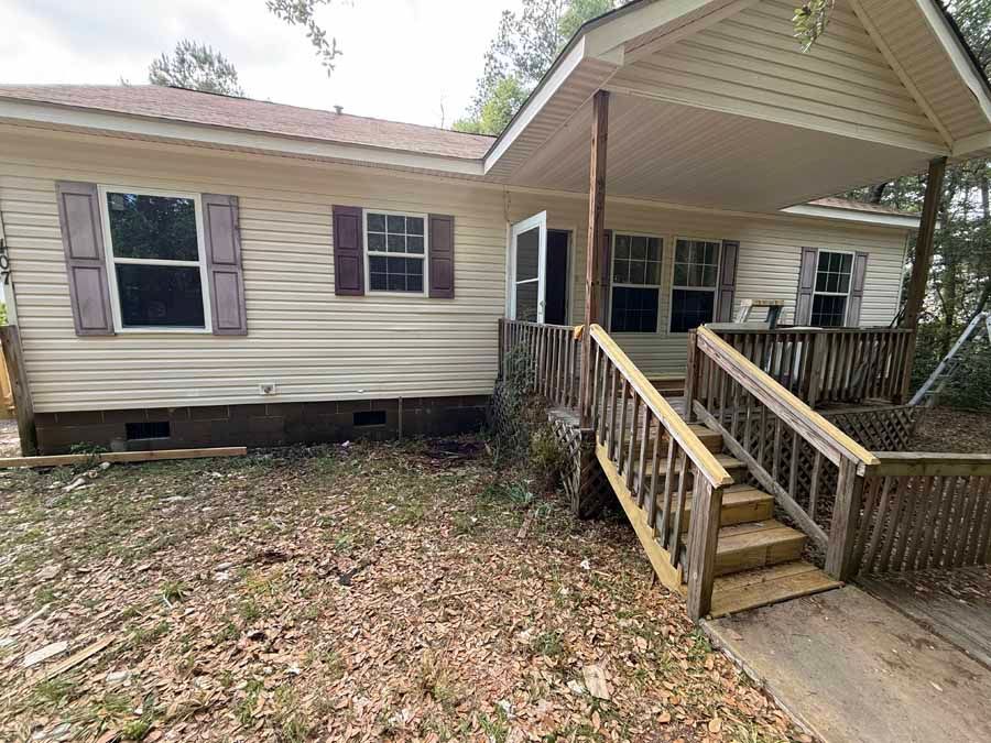 Single-story beige house with front porch and steps leading to the entrance, surrounded by leaf-covered yard.