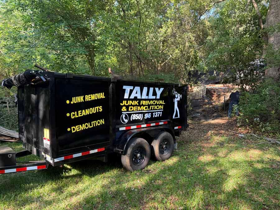 Black Tally junk removal trailer parked by trees, with yellow service text on the side.