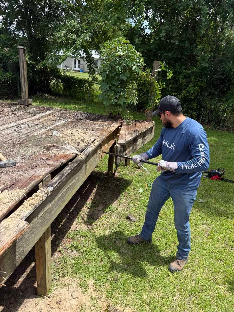 Man inspecting a damaged wooden deck outdoors beside trees and grass