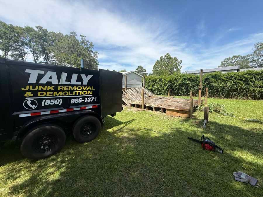 Junk removal truck parked beside a wooden trailer in a grassy yard on a sunny day