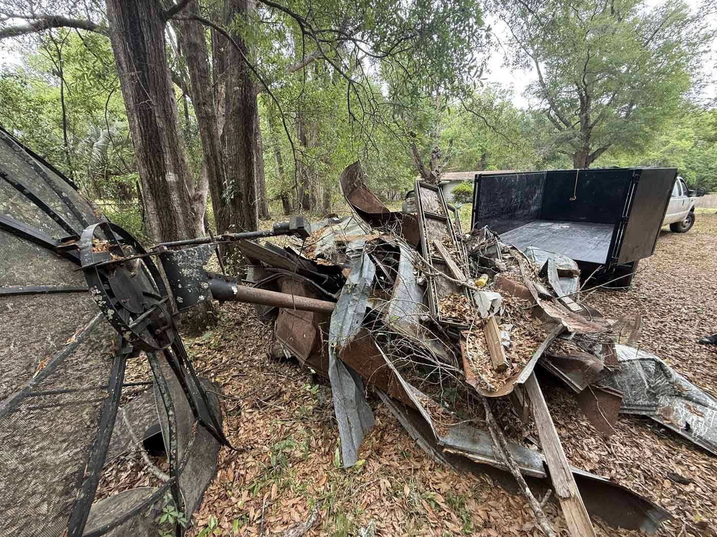 Twisted metal debris and a damaged black vehicle in a wooded area.