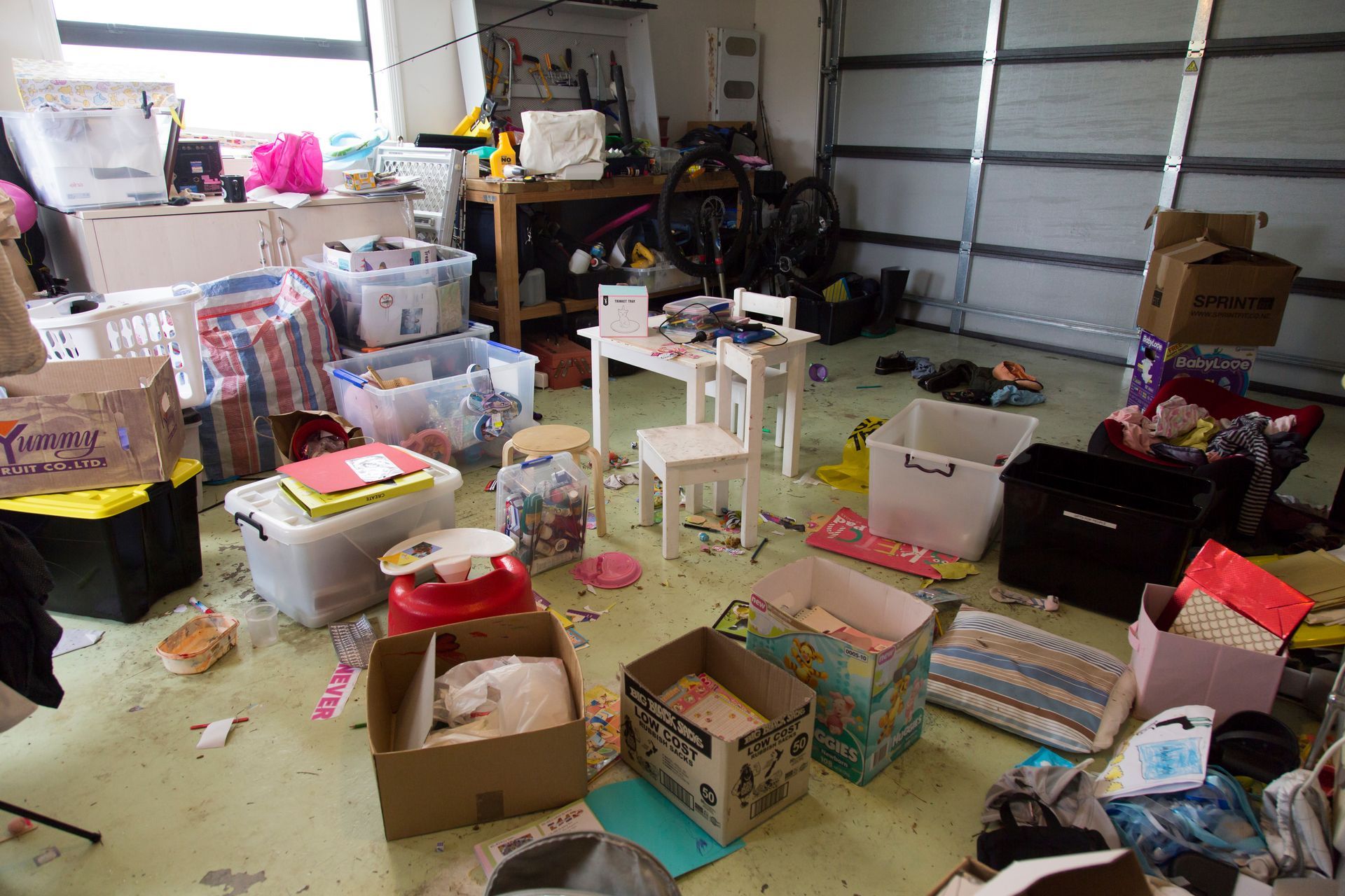 Cluttered garage with boxes, bins, toys, and household items scattered across the floor.
