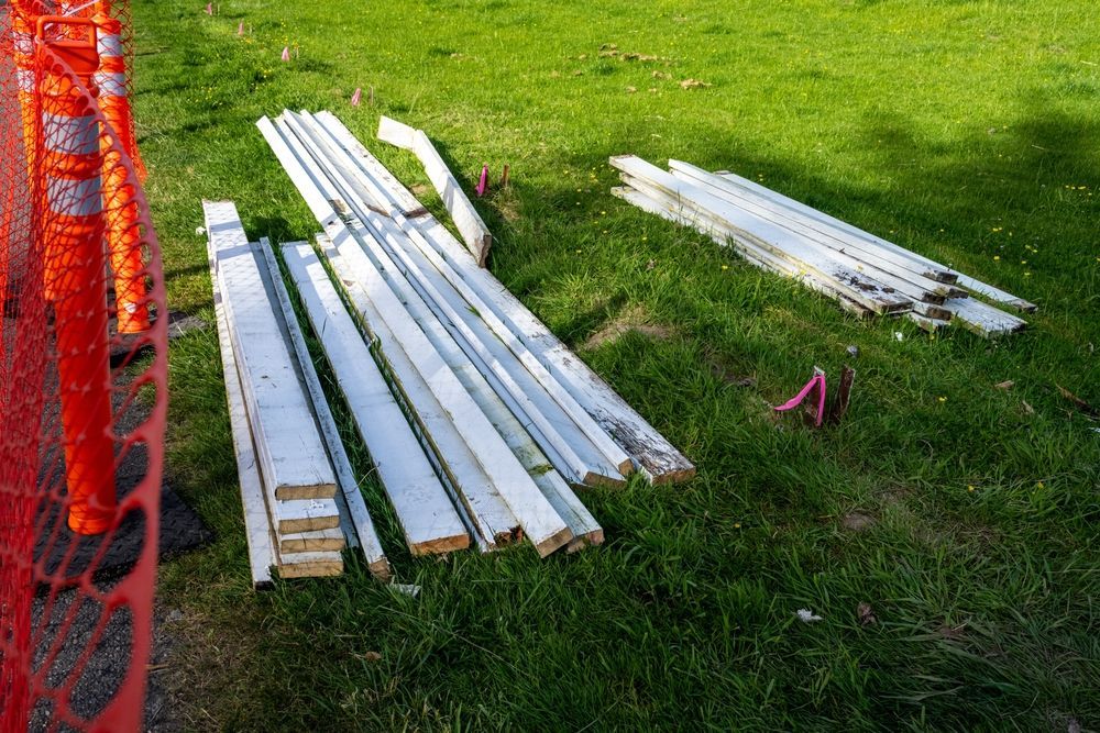White lumber planks laid out on green grass beside an orange fence and a small pink object