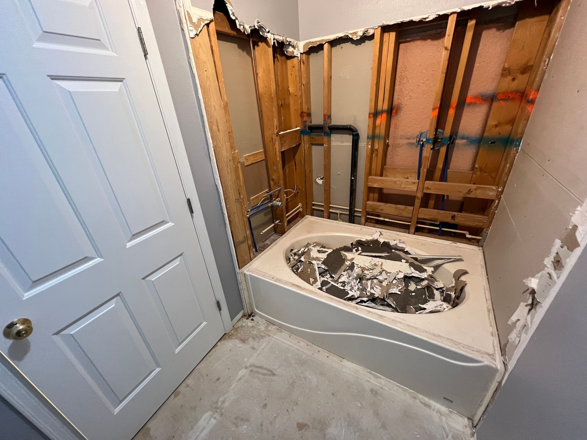 Bathroom under renovation with exposed wall framing and a removed bathtub.