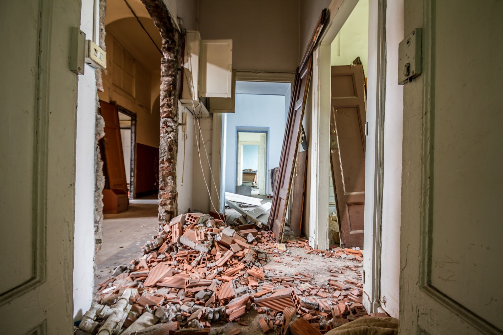 Damaged hallway with rubble and debris strewn across the floor, leading to a room in the distance