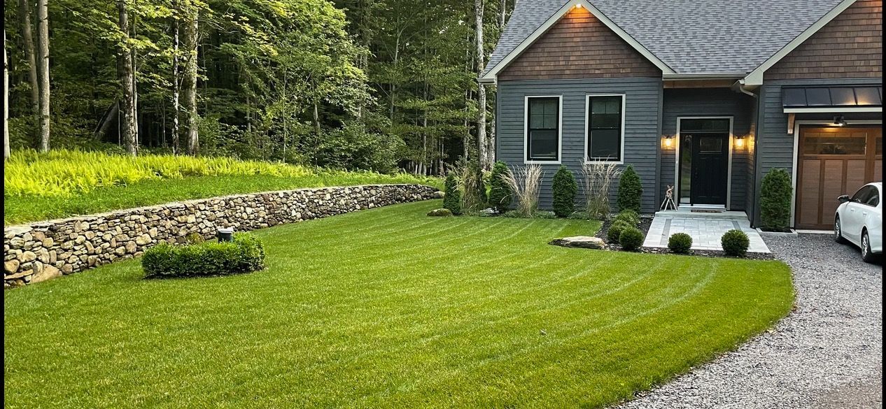 Une maison avec une voiture garée devant et une pelouse verte luxuriante.