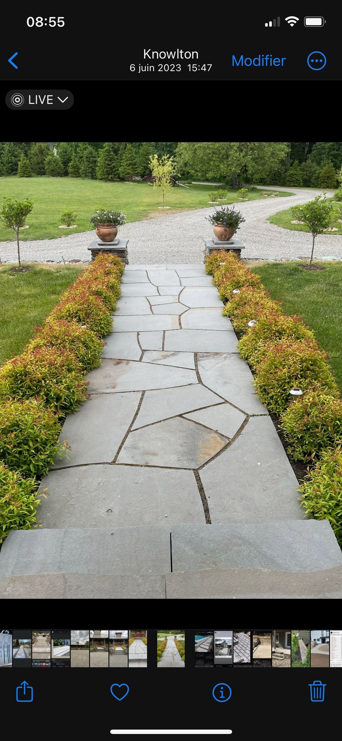 Un écran de téléphone montre une allée en pierre bordée de fleurs et d'arbustes.