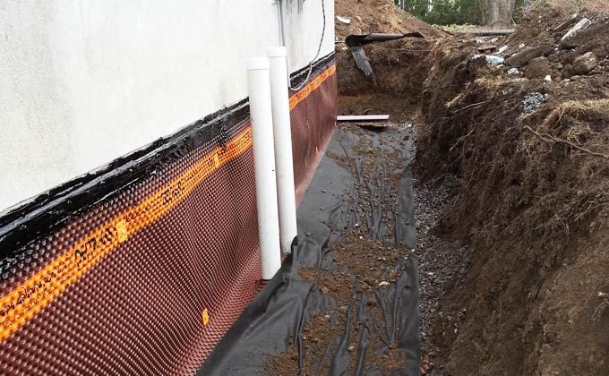 Un système de drainage est en cours d'installation sur le côté d'un bâtiment.