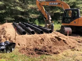 Une excavatrice est assise sur un tas de terre à côté d'un tas de tuyaux.