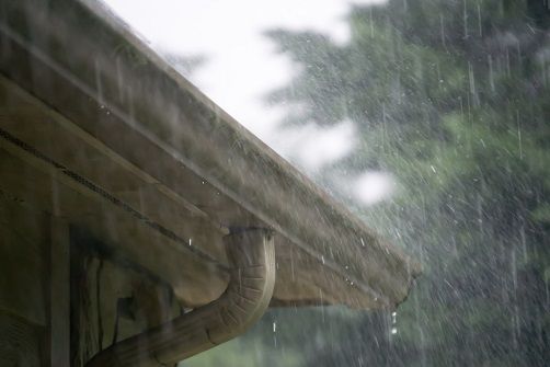Rain pouring from a building's gutter, highlighting the downpour in an outdoor setting.
