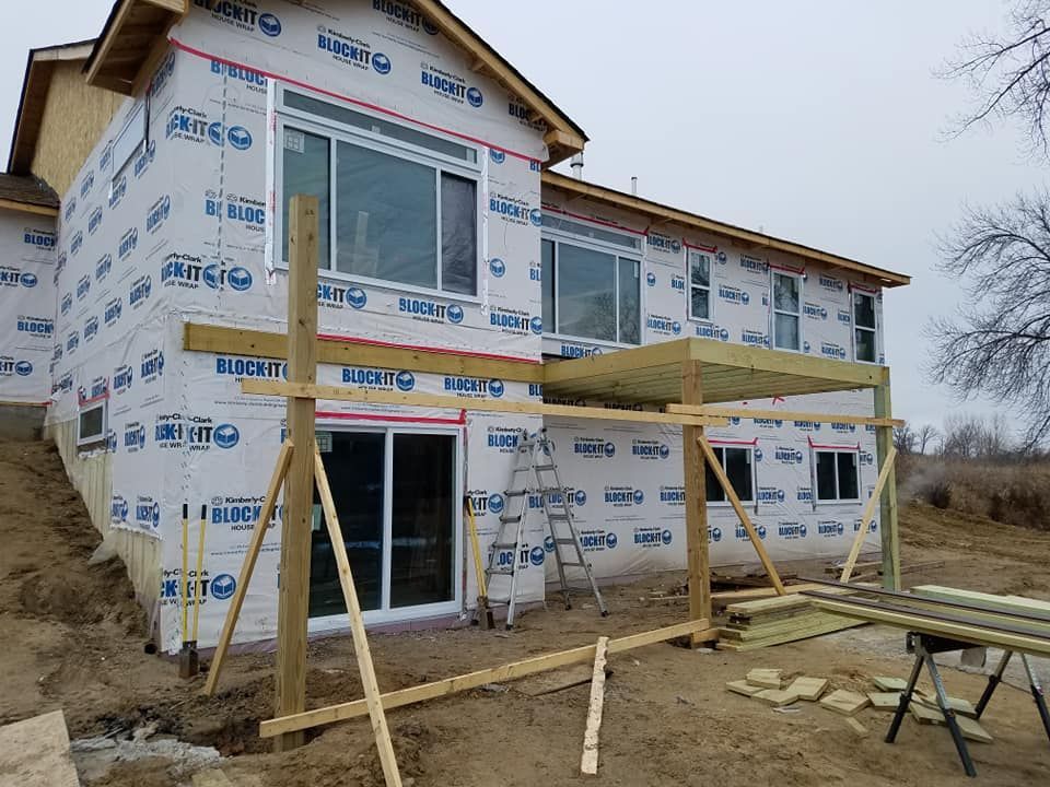 Two-story house under construction, a partially built deck. Exterior walls covered in protective wrap.