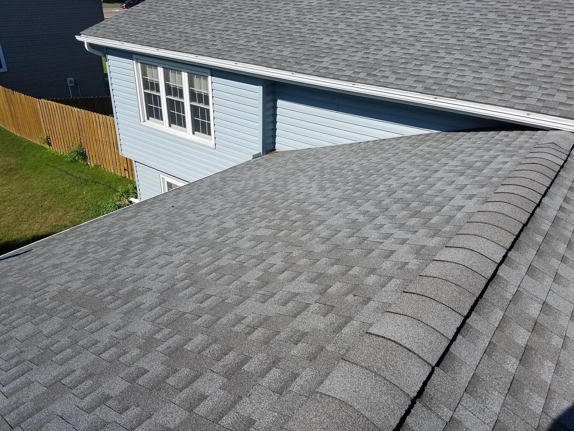 Gray shingled roof of a light blue two-story house with white trim, viewed from above.
