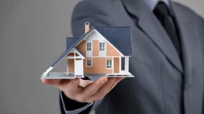 A man in a suit is holding a model house in his hand.