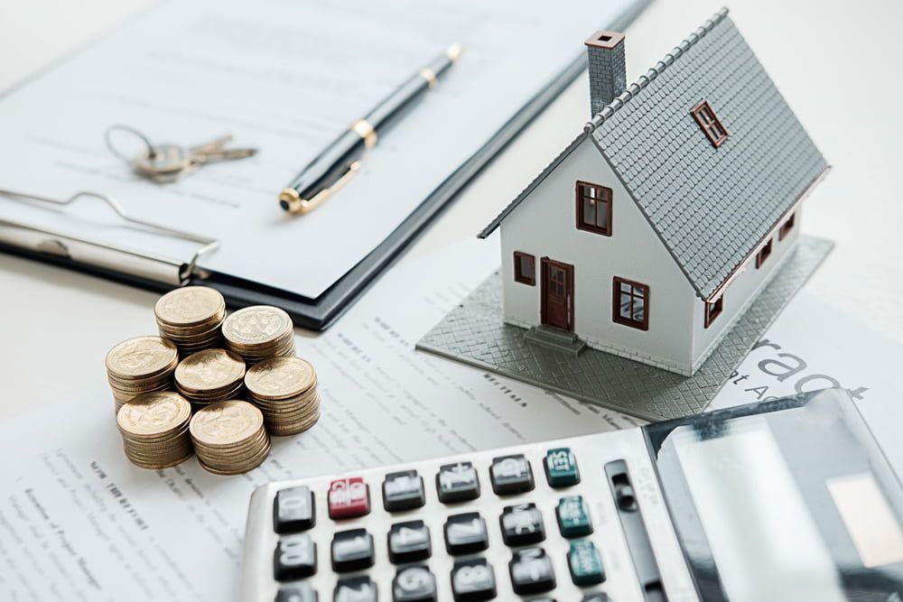 A Model House on Top of A Pile of Coins Next to A Calculator — As Is Where Is in Auckland, NZ