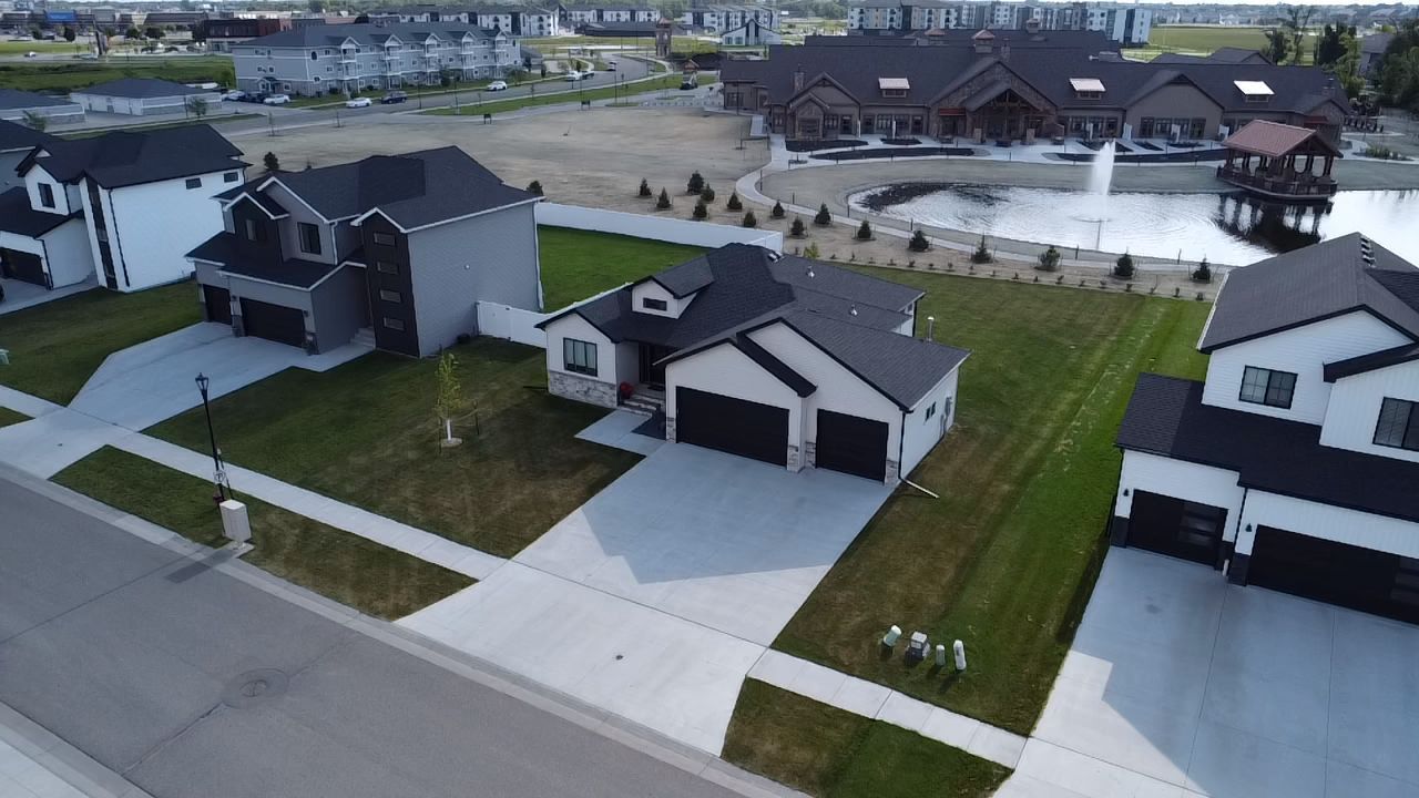 An aerial view of a suburban neighborhood with modern single-family homes, green lawns, and a nearby pond with a fountain.