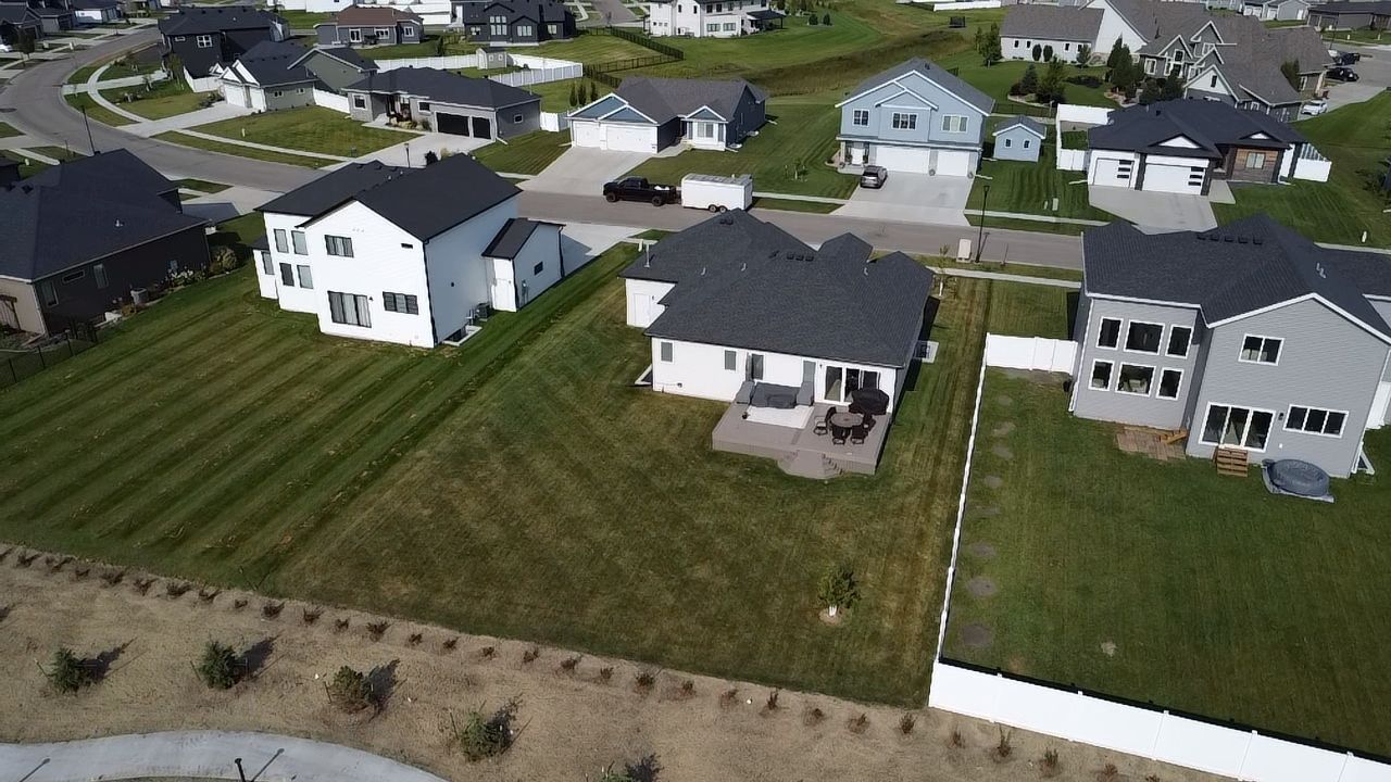 An aerial view of a suburban neighborhood showing detached houses with manicured lawns and paved streets.
