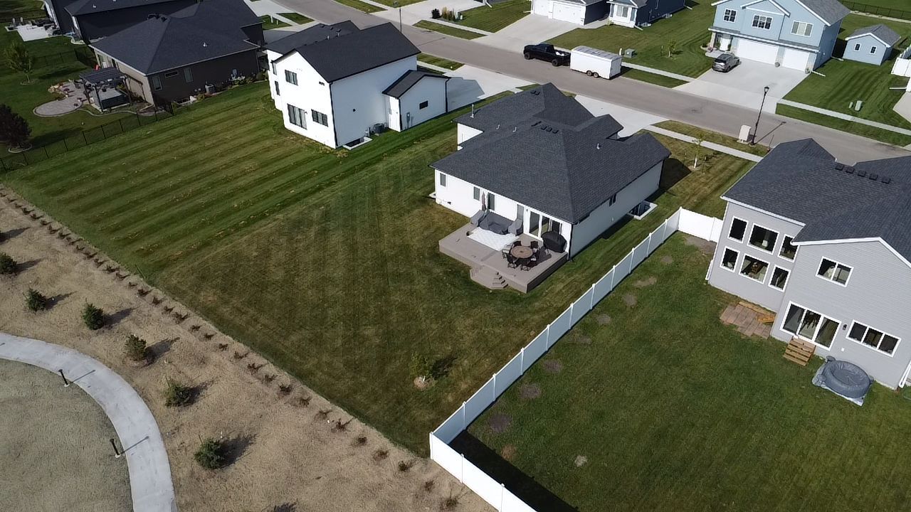 Aerial view of a residential neighborhood featuring houses with green lawns, driveways, and a white fence.