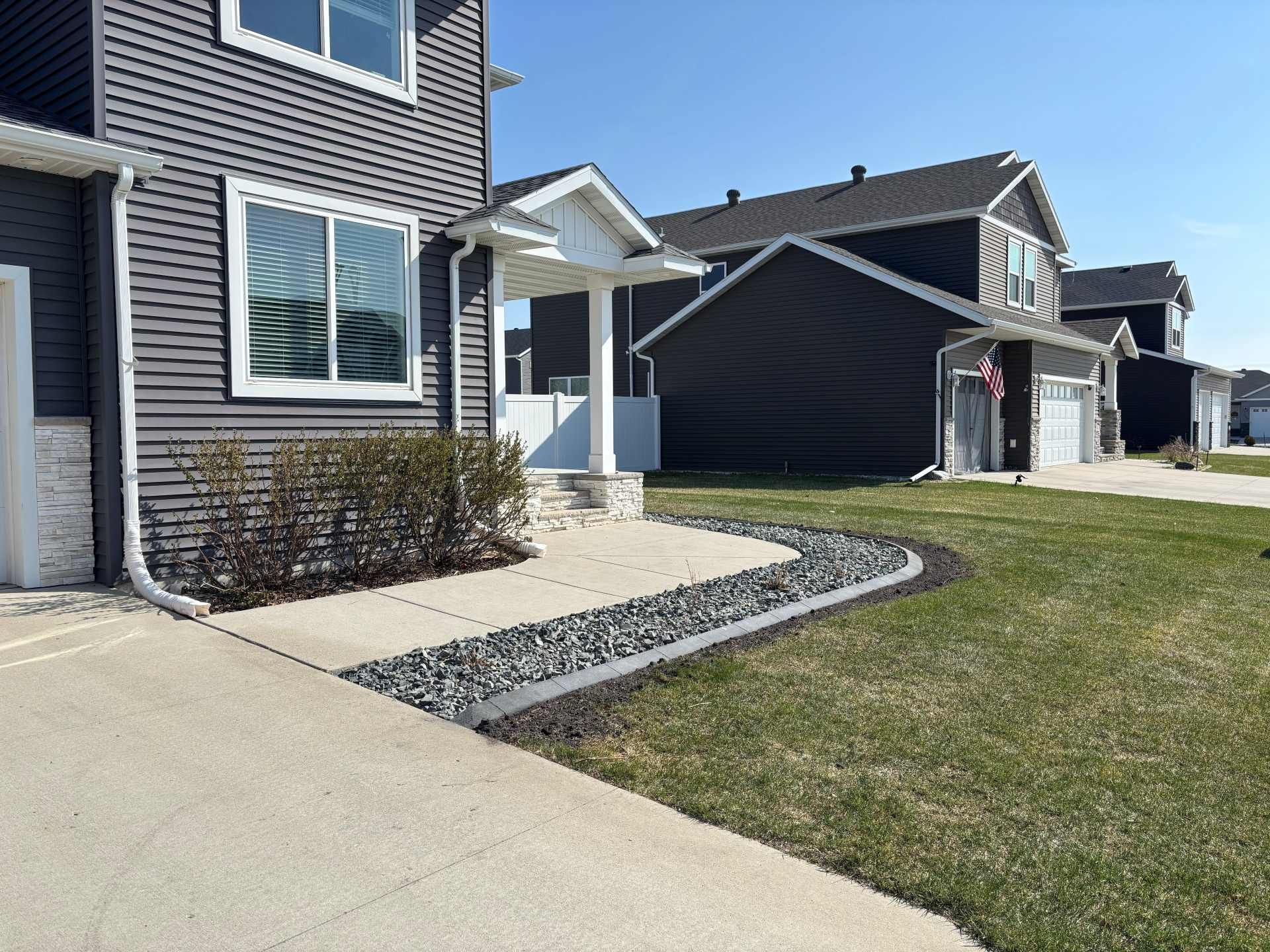 A suburban home with dark grey siding, a front porch, and a stone-bordered garden bed with grey river rocks.