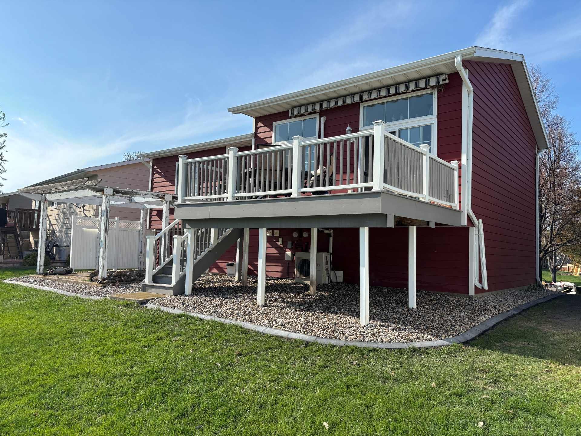 Red house exterior featuring a raised wooden deck with white railings, a small staircase, and a graveled backyard.