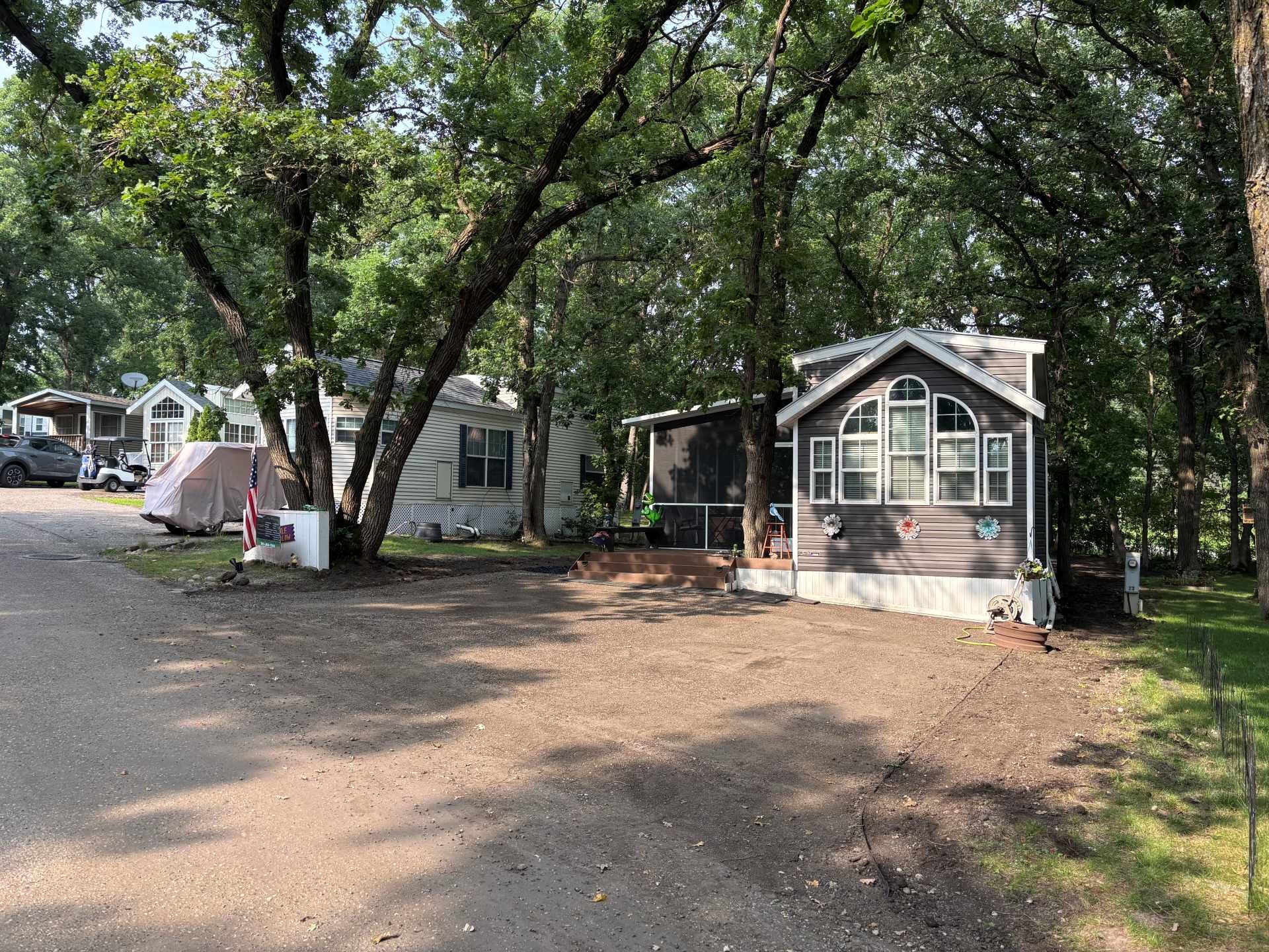 A gravel driveway leading to two small cabins nestled under tall, leafy trees on a bright day.