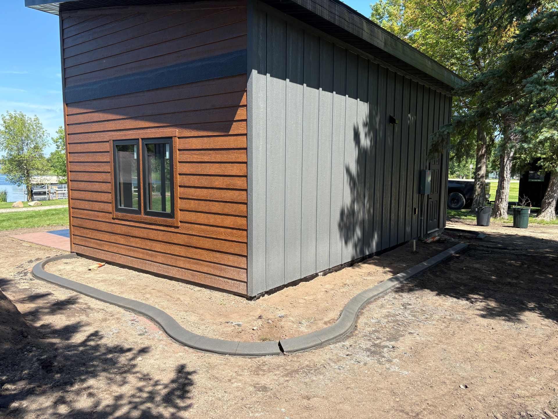 A modern cabin corner featuring brown wood-paneled and gray vertical siding, framed by a curved concrete landscape border.